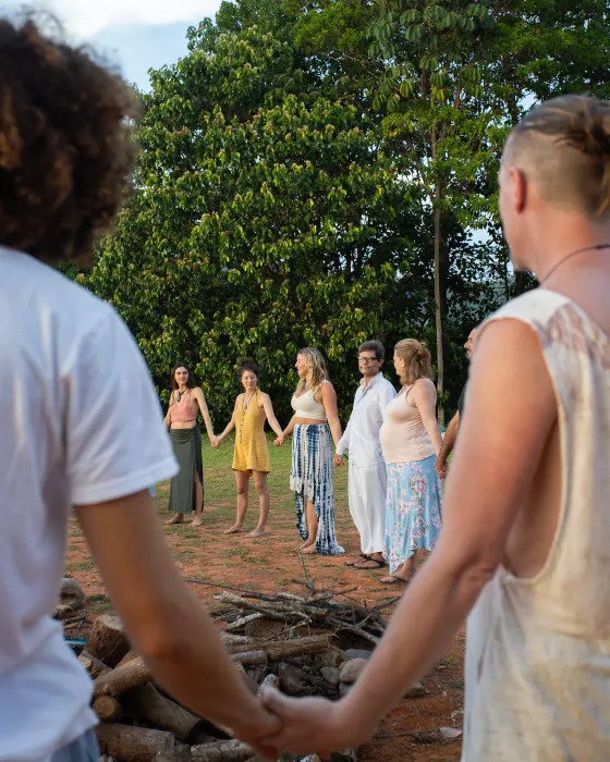 The village holding hands in a circle around the unlit fire at Amora, seen between two clasped hands in the foreground.