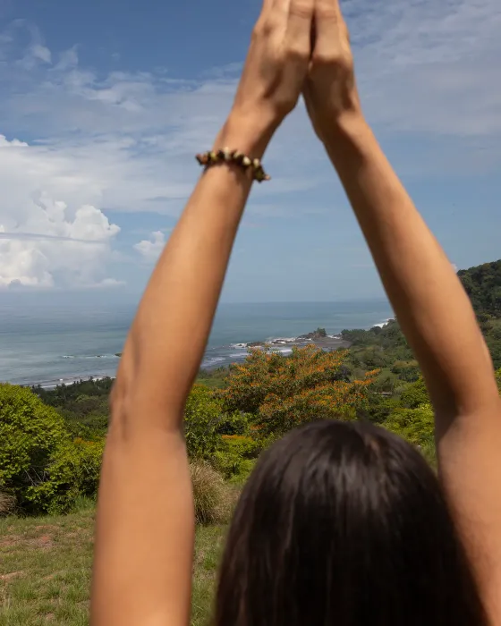 A woman with her palms pressed together above her head, facing the ocean from the ridge at Amora, an ocean-view community on the Costa Ballena.