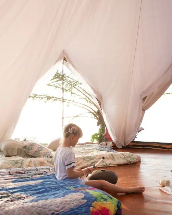 A child sitting on sleeping mats inside a bright bell tent on the land at Amora, Dominicalito.