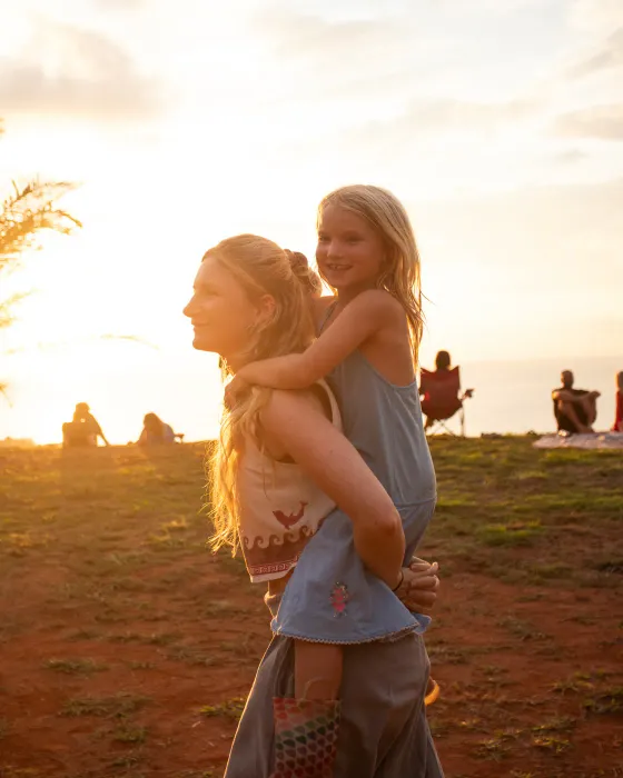 A girl riding on a woman's back at a sunset gathering on the ridge at Amora, close to Dominical, Costa Rica.